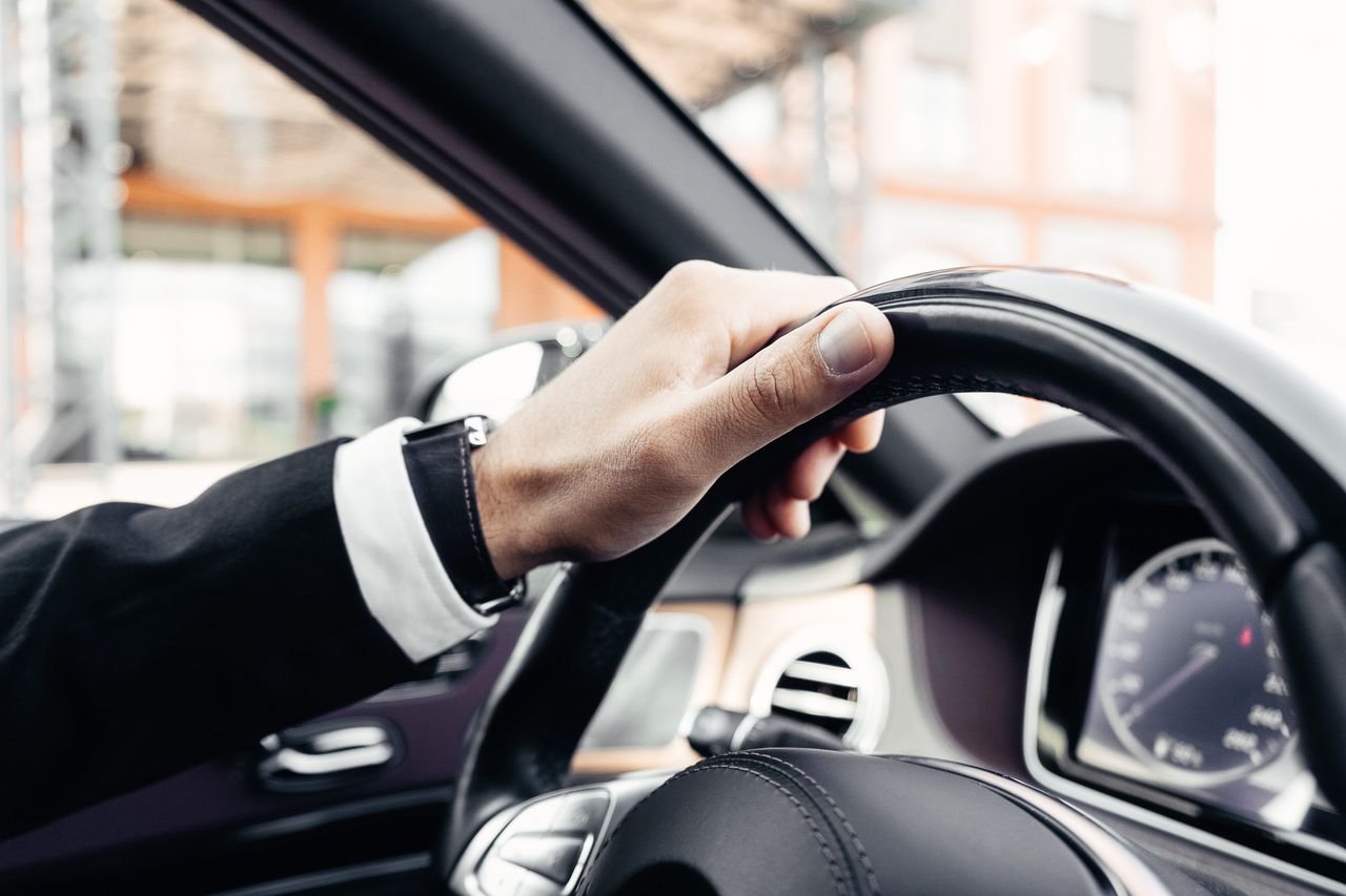 Elegant hand in a suit holding a modern car steering wheel, close-up shot inside a vehicle.