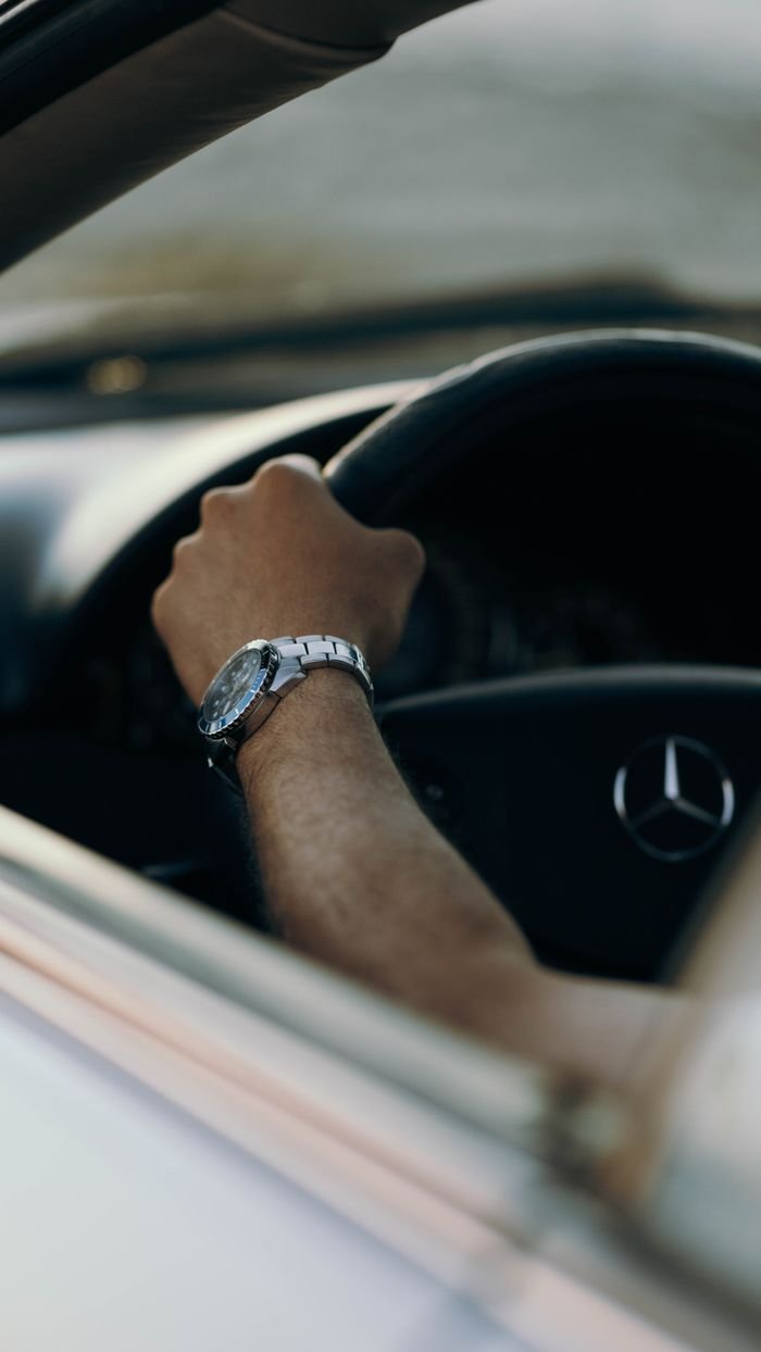 A hand wearing a silver watch grips a Mercedes-Benz steering wheel, showcasing luxury driving in Libya.