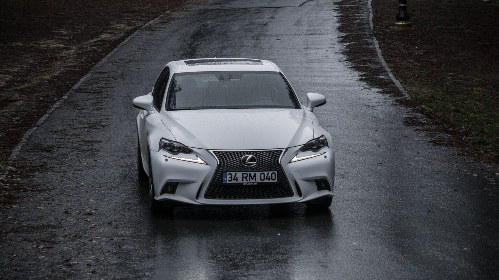 Front view of a white Lexus car driving on a rain-soaked road.