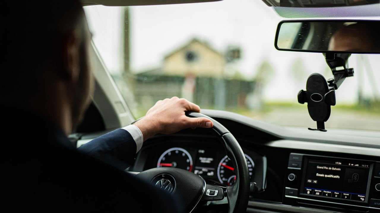 Businessman in suit driving a car, focus on steering wheel and dashboard.