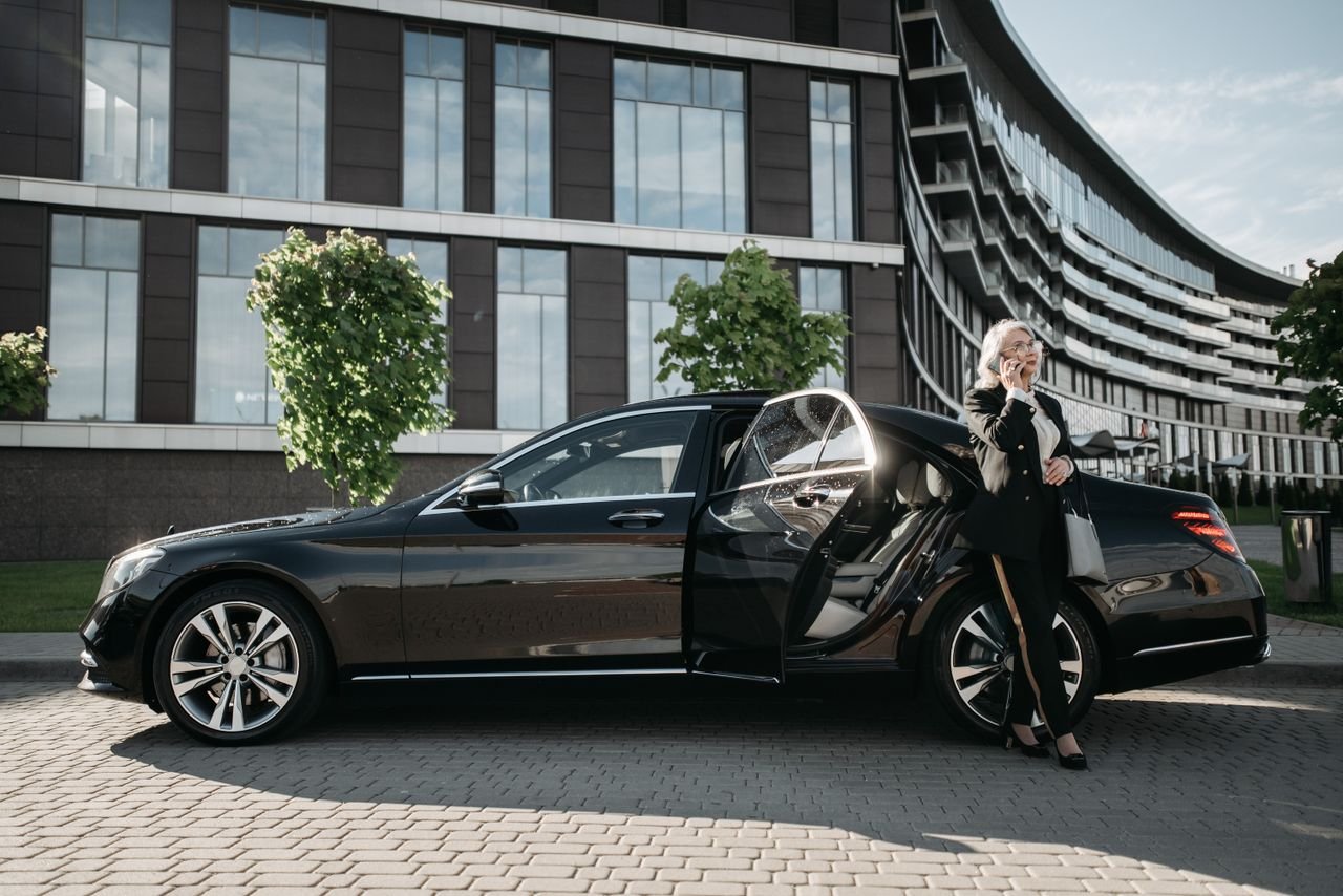 Confident businesswoman in suit using cellphone beside luxury car downtown.